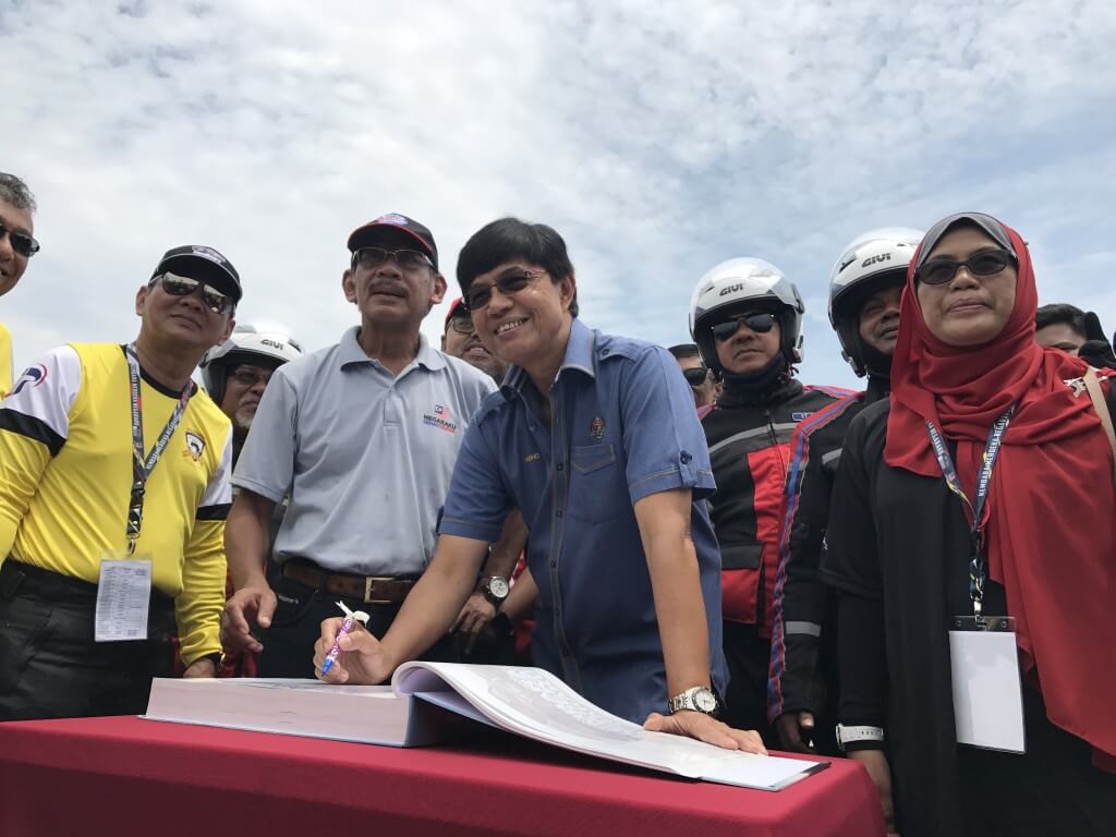 ADUN Penaga, Datuk Mohd Zain Ahmad menandatangani buku KMN 2017 sambil diperhatikan oleh Ketua Konvoi, Ariah Judah (kanan)