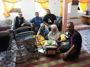 Mohd Kassim dan isteri memegang kerusi roda sambil tersenyum syukur atas keperihatinan kerajaan persekutuan.