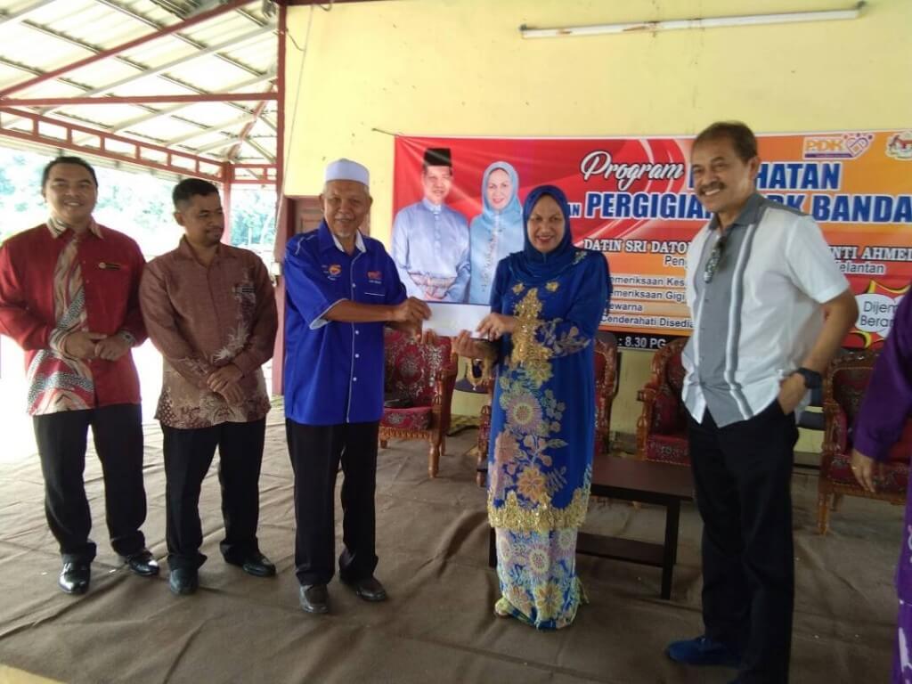 Mat Abu Hamat (berbaju biru) menerima cek RM 5 ribu dari Khamarzan sambil diperhatikan oleh Pegawai JKM Jeli, Saiful Nizam (berbaju batik coklat).