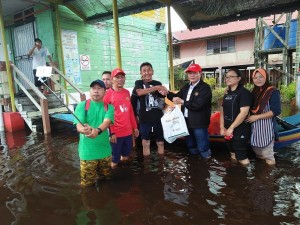 Suleihei (bertopi merah) menyampaikan sumbangan barangan makanan kepada Deli Neng (empat kiri) di tangga bangunan sekolah yang tenggelam.  