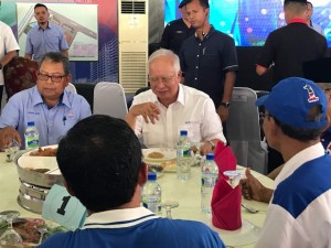 Awang Adek (kiri) ketika mengiringi Najib ( tengah) beramah mesra dengan penduduk setempat di meja hidangan.