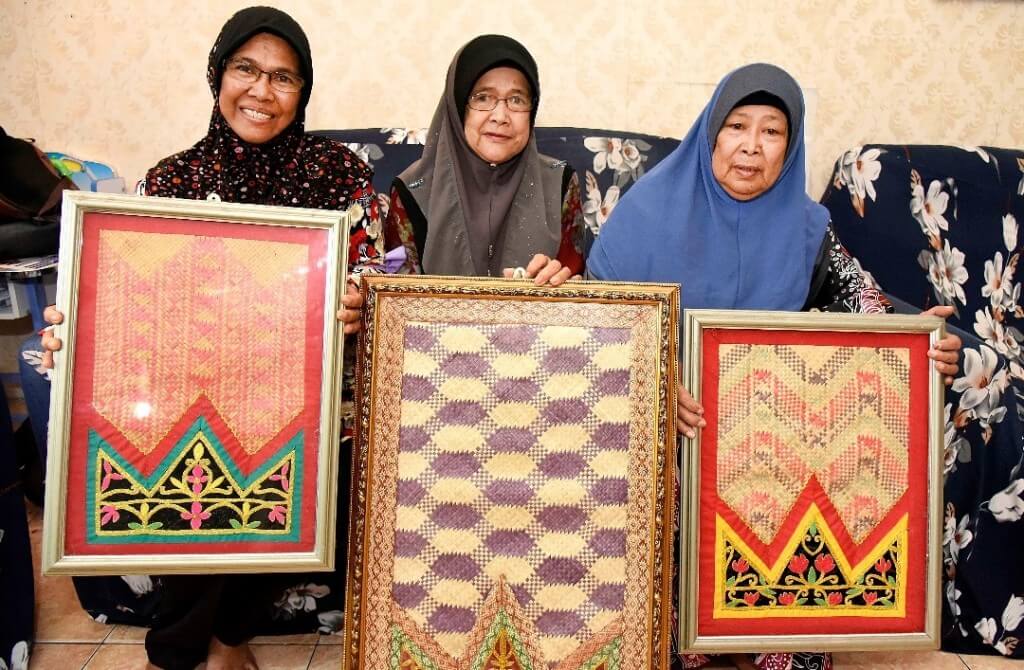Siti Nabiah, Siti Hawa dan Siti Miah bangga menunjukkan tikar baju hasil kerja tangan mereka.