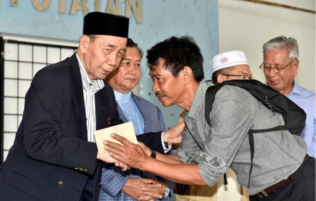 Hasbullah (kiri) menyampaikan sumbangan dari Pusat Zakat Sabah kepada salah seorang ketua keluarga, Mazlan Musa (kanan) pada majlis penyampaian sumbangan tersebut