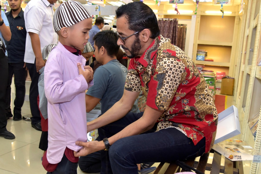 Mohamad Amran membantu salah seorang anak MAWIS memakaikan baju raya.