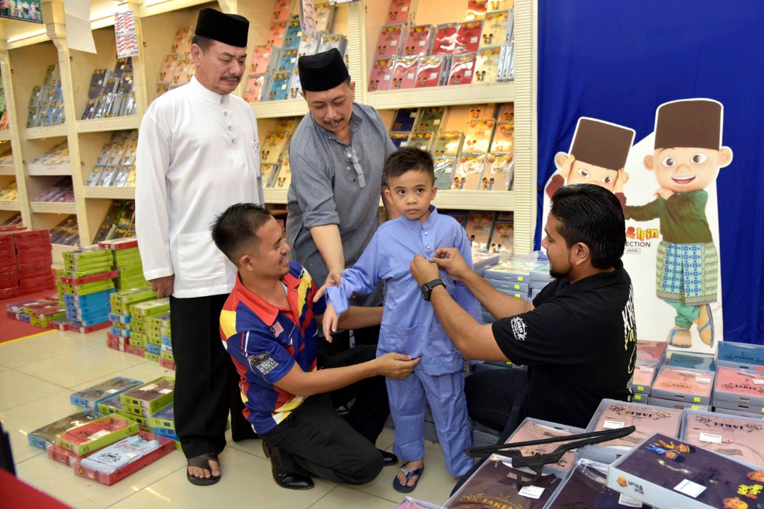 Danish Ilham dibantu Badrul (duduk kiri) dan Yunus (dua dari kiri) mencuba Baju Melayu jenama Upin Ipin. 