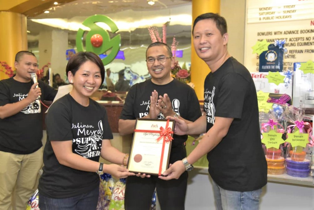 5.George (kanan) menyampaikan sijil penyertaan kepada Ketua Penolong Pengarah Media dan Komunikasi Korporat, Jabatan Penerangan Sabah, Imelda Godon (kiri) sambil disaksikan Samsuni (tengah)