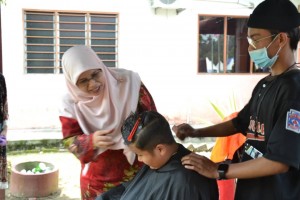 Rodziah (kiri) melihat aktiviti gunting rambut percuma sempena Program Sayangi Desa di Felda Sungai Tengi.