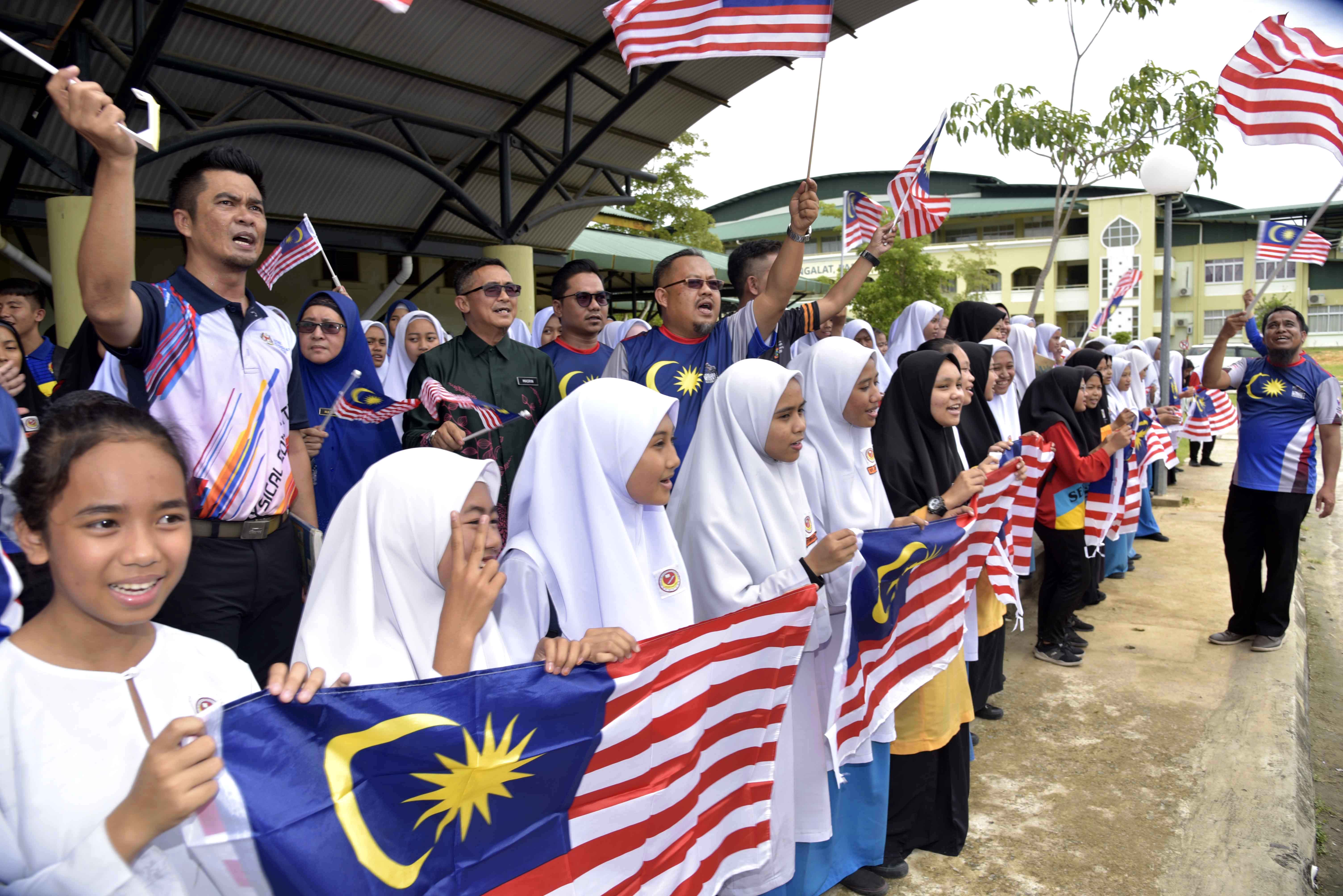 Kelihatan Zulhanin mengibarkan bendera bersama pelajar-pelajar sekolah. 