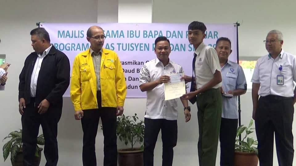 Liechet (Tengah) menyampaikan bantuan wang Saku sekolah kepada pelajar Tuisyen SPM 2019 tajaan Petronas (Kanan) 