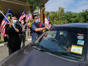 Pegawai Penerangan Daerah Kemaman melekatkan Jalur Gemilang pada kenderaan ketika acara pelepasan Konvoi Merdeka disaksikan oleh Pengarah KKTM.