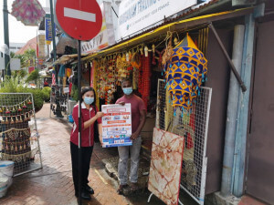 Wakil Pegawai Pejabat Penerangan DTL membantu peniaga kedai menampal poster di kawasan Little India.