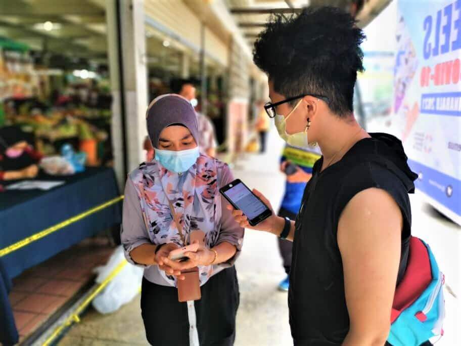 Hasmawati (kiri) membantu salah seorang warga Kota Kinabalu untuk mendaftarkan diri sebagai penerima vaksin menggunakan aplikasi MySejahtera di Pasar Besar Kota Kinabalu.