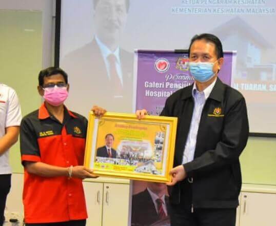 Dr. G Mohan (kiri) menyampaikan cenderahati kepada Noor Hisham (kanan).