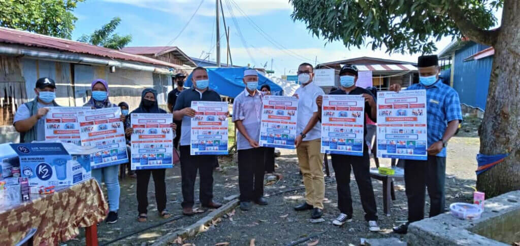 Jusman (empat dari kanan) menyampaikan poster kempen pembudayaan norma baharu kepada penduduk di Kampung Kasnuri.