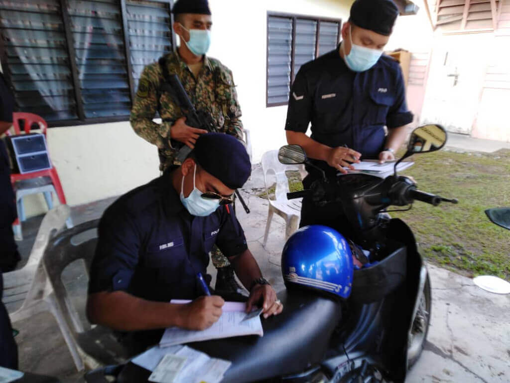 Anggota polis sedang mengeluarkan kompaun yang dikenakan kepada tuan rumah dan tetamu yang melanggar SOP Aidilfitri di Kampung Kenanga, Rawang.