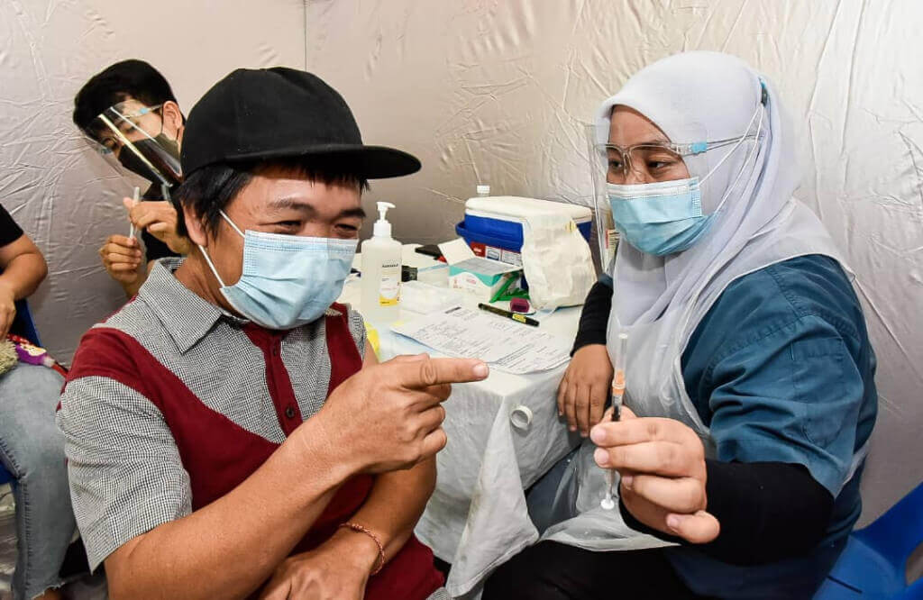 Juruvaksin bertugas (kanan) menunjukkan jarum vaksin kepada penerima suntikan sebelum disuntik.