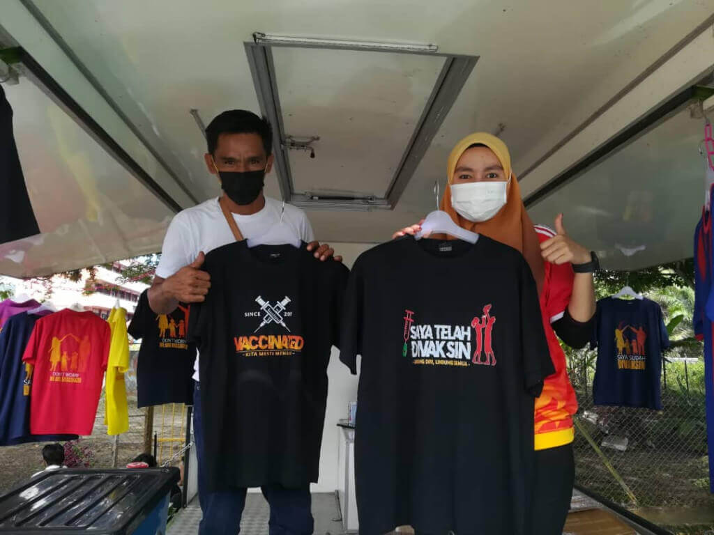 Muhamad bersama pekerjanya, Effa Syuhada Basrah (kanan) menunjukkan baju yang dijual yang direka khas untuk penerima vaksin.