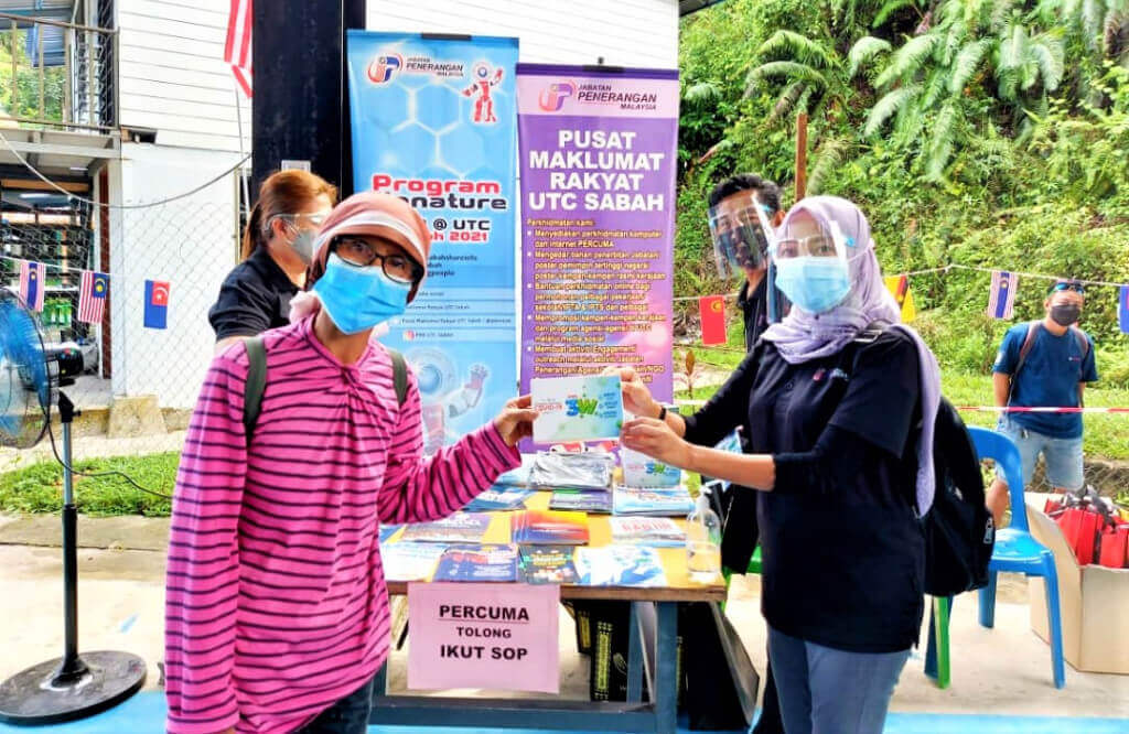 Sabina Gadaul (kiri) menerima bahan penerbitan dan cenderahati dari Pegawai Pusat Maklumat Rakyat Kota Kinabalu, Norayah Ganipin.