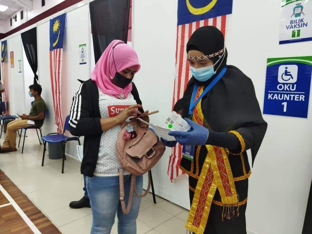 (Kanan) Nurul Fatin sedang melayan seorang penerima vaksin dengan mengenakan pakaian etnik Kadazan semasa bertugas di PPV UniKL hari ini.