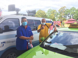 Khairul Mahadi Ahmad (kanan) bersama Pegawai Penerangan Daerah Setiu, melekatkan Jalur Gemilang kepada salah sebuah teksi.