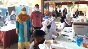 Pengetua SMKDHHY dan YDP PIBG melihat pada petugas kesihatan menjalankan proses pemberian vaksin.