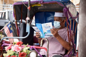 Pengayuh beca tekun membaca risalah dasar-dasar kerajaan yang diedarkan oleh Pejabat Penerangan Daerah Kuala Terengganu.