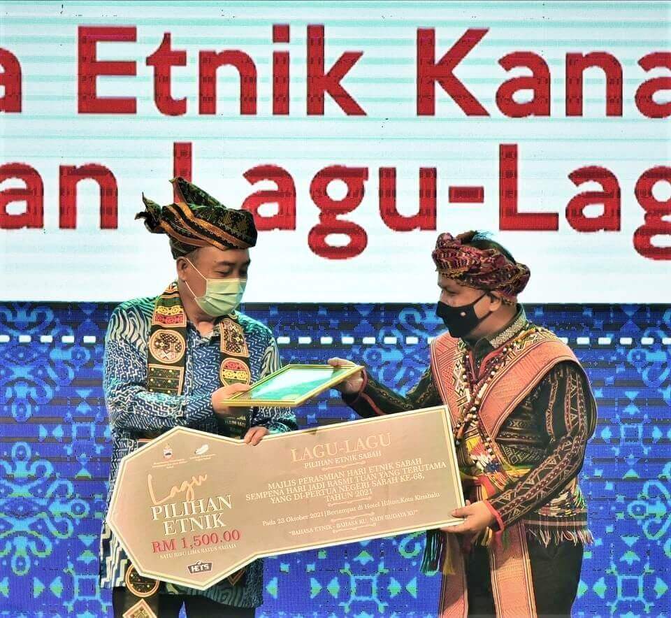 Hajiji (kiri) menyampaikan hadiah Pertandingan Lagu-lagu Pilihan Etnik Sabah 2021 kepada Datuk Jelani Hamdan.