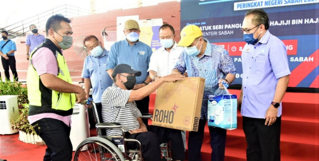 Gambar Hajiji (tengah) menyampaikan peralatan pemulihan dan insurans PERKESO kepada salah seorang penerima.