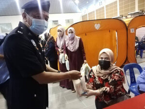 Ketua Balai Polis daerah mengagihkan buah tangan buat penerima dos kedua AstraZeneca, Che Ani Ahmad.